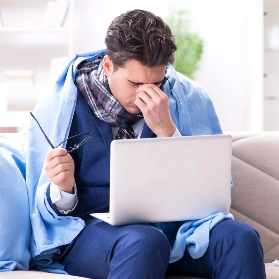 Unwell man in a scarf and blanket sitting with a laptop