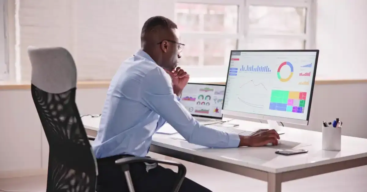 Man reviewing colourful dashboard charts on a desktop monitor and laptop