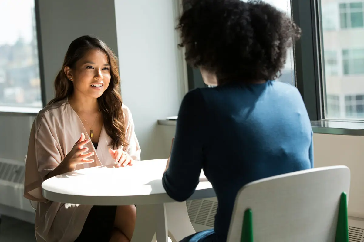 Two women talking across a small table in a bright office